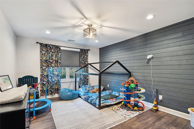 bedroom with recessed lighting, wood walls, baseboards, and wood finished floors