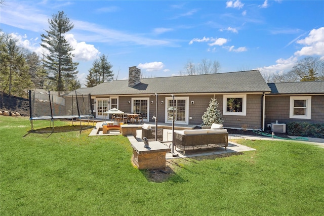 rear view of property featuring a trampoline, a lawn, a chimney, and an outdoor hangout area