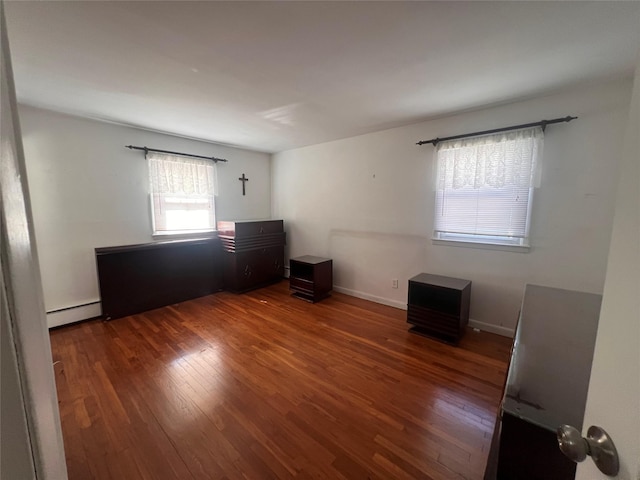 unfurnished bedroom with wood finished floors, baseboards, and baseboard heating