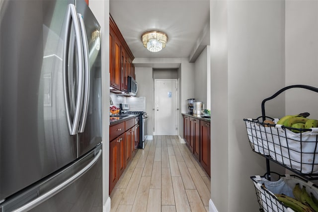 kitchen with light wood-type flooring, dark countertops, stainless steel appliances, dark brown cabinets, and a chandelier