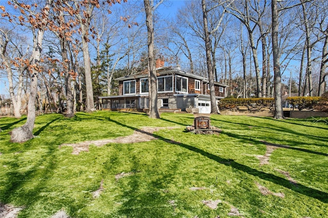 rear view of house with a lawn, a chimney, a garage, and a sunroom