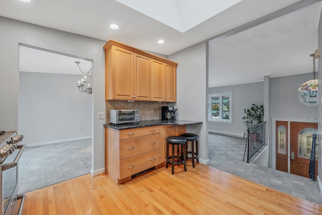 kitchen with light wood-style flooring, a toaster, stainless steel stove, a baseboard heating unit, and tasteful backsplash