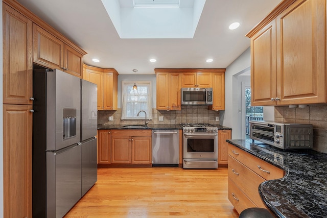 kitchen featuring decorative light fixtures, a toaster, light wood-type flooring, stainless steel appliances, and a sink