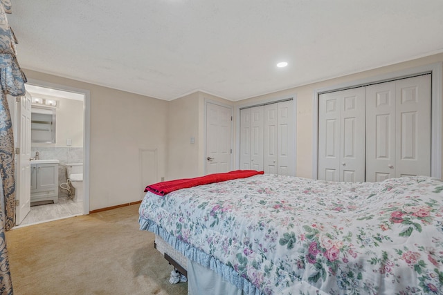 bedroom featuring light colored carpet, baseboards, two closets, and ensuite bath