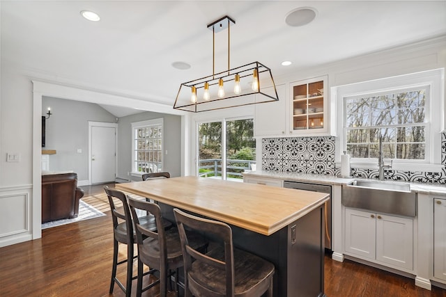 kitchen with white cabinets, hanging light fixtures, a kitchen breakfast bar, lofted ceiling, and glass insert cabinets