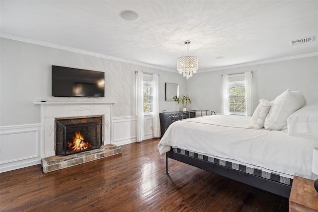 bedroom featuring a lit fireplace, visible vents, crown molding, wood finished floors, and a wainscoted wall