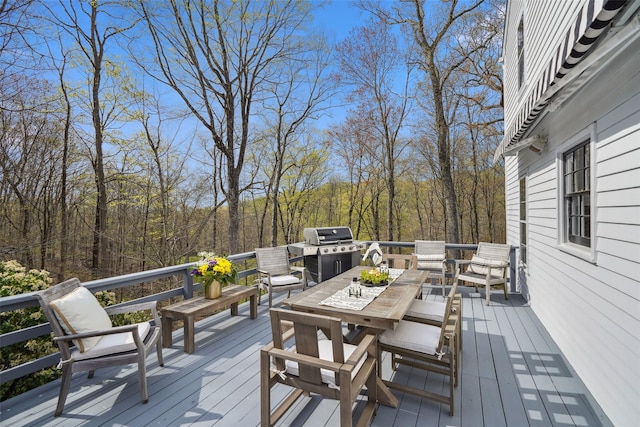 wooden deck featuring a view of trees, outdoor dining area, and a grill
