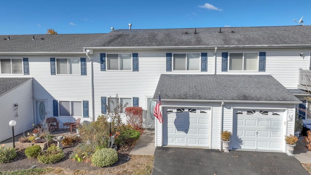 rear view of property with an attached garage, driveway, and roof with shingles