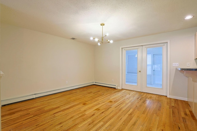 empty room with visible vents, light wood-type flooring, baseboard heating, a notable chandelier, and a baseboard radiator