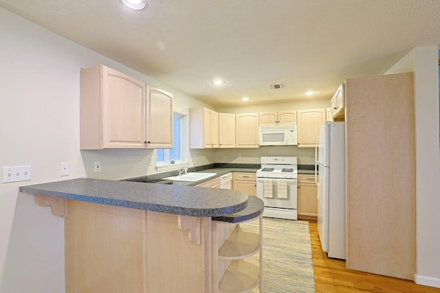 kitchen with a sink, a kitchen breakfast bar, white appliances, and a peninsula