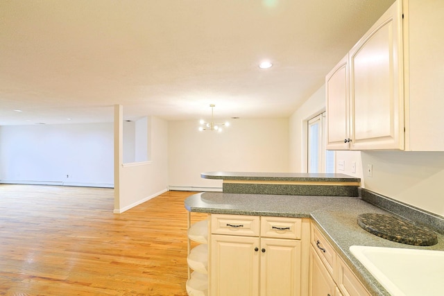 kitchen featuring open floor plan, light wood-style floors, a peninsula, an inviting chandelier, and baseboard heating