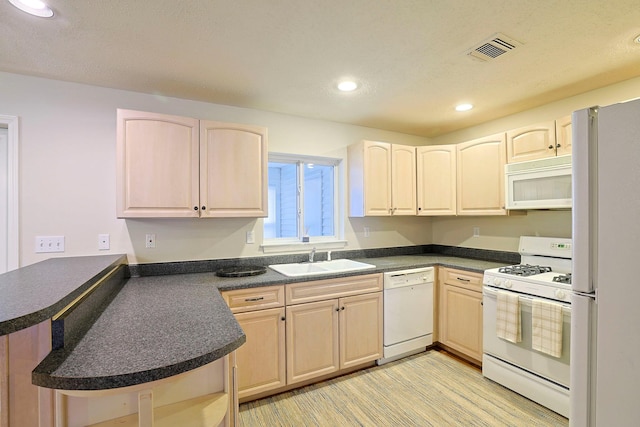 kitchen with visible vents, light brown cabinetry, a sink, dark countertops, and white appliances