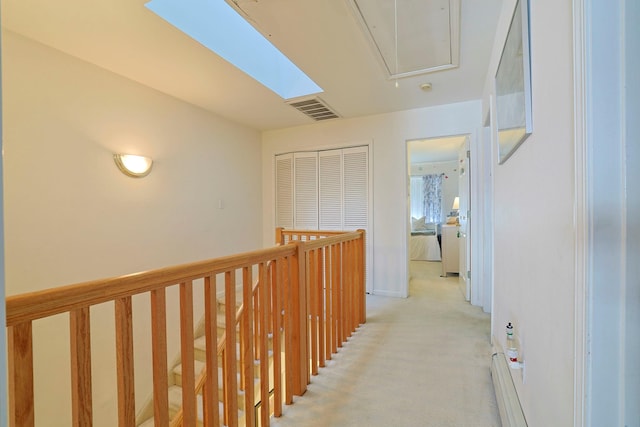 corridor with a baseboard heating unit, attic access, light colored carpet, and visible vents