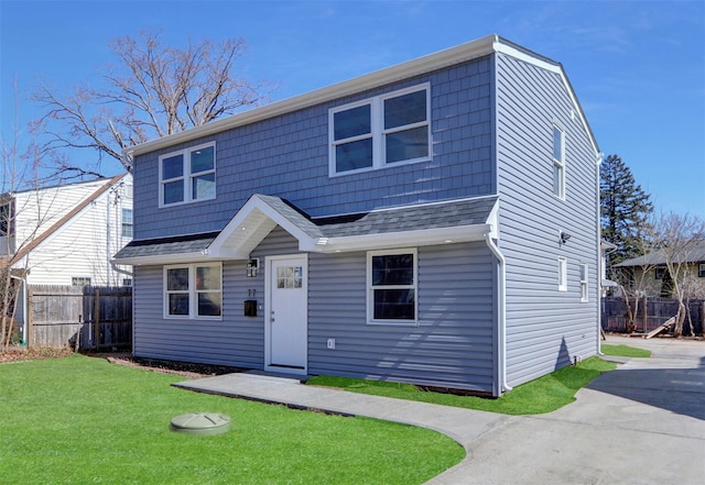 view of front facade featuring concrete driveway, a front yard, roof with shingles, and fence