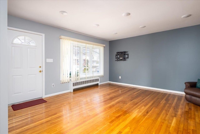 foyer entrance with radiator, baseboards, and light wood-type flooring