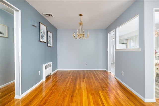 spare room with visible vents, baseboards, a chandelier, radiator heating unit, and wood finished floors