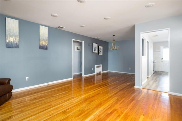 unfurnished living room with radiator, baseboards, visible vents, light wood finished floors, and a notable chandelier