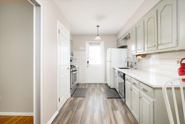 kitchen with baseboards, light countertops, wood finished floors, stainless steel appliances, and a sink