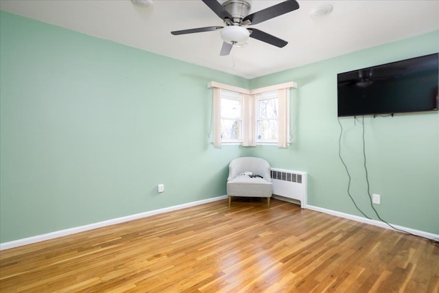 unfurnished room with a ceiling fan, baseboards, light wood-style floors, and radiator heating unit