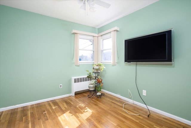 interior space with a ceiling fan, radiator heating unit, baseboards, and wood finished floors