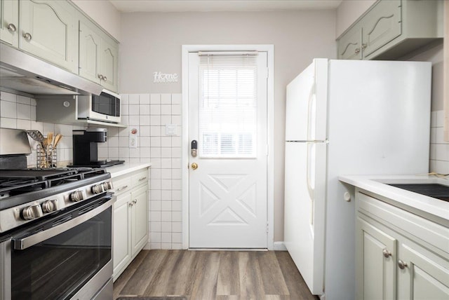 kitchen featuring under cabinet range hood, wood finished floors, white appliances, tile walls, and light countertops