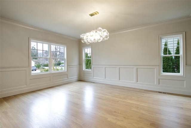 spare room featuring light wood finished floors, visible vents, crown molding, an inviting chandelier, and a decorative wall