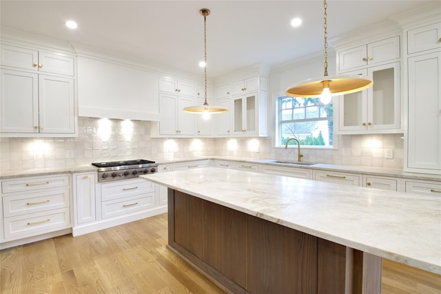 kitchen with light wood-type flooring, a sink, stainless steel gas stovetop, white cabinets, and glass insert cabinets