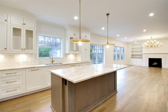 kitchen with white cabinetry, crown molding, a kitchen island, and a sink