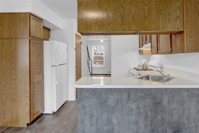 kitchen featuring under cabinet range hood, light countertops, a peninsula, white appliances, and a sink