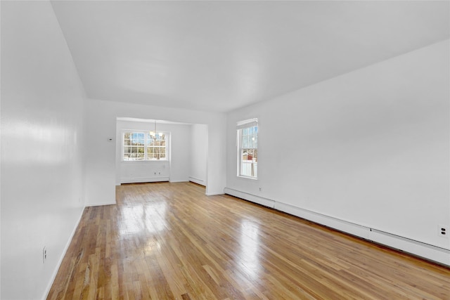 empty room with a notable chandelier, baseboard heating, baseboards, and light wood-style floors