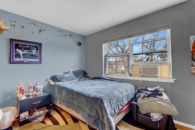 bedroom with cooling unit, baseboards, and wood finished floors