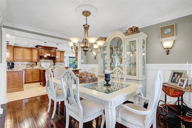 dining space featuring a decorative wall, a wainscoted wall, ornamental molding, wood finished floors, and a notable chandelier