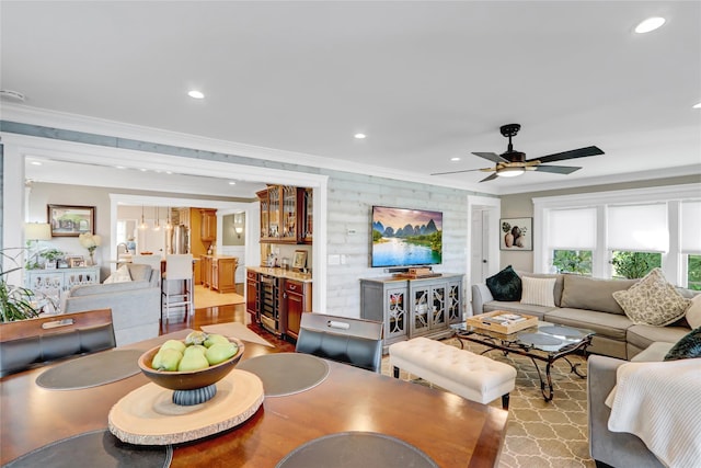 living area featuring beverage cooler, ornamental molding, recessed lighting, bar area, and ceiling fan