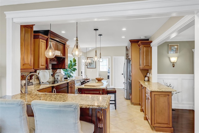 kitchen with a kitchen island, light stone counters, a peninsula, a kitchen breakfast bar, and freestanding refrigerator