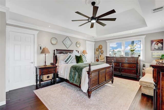 bedroom featuring visible vents, ornamental molding, hardwood / wood-style flooring, a tray ceiling, and ceiling fan