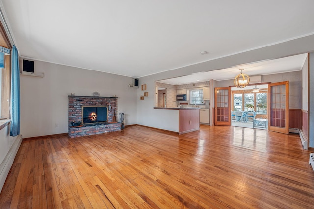 unfurnished living room with baseboards, a baseboard radiator, an inviting chandelier, light wood-style flooring, and a brick fireplace