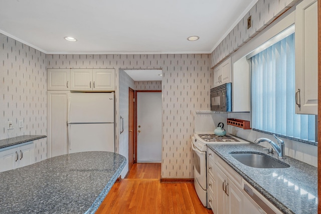 kitchen featuring white appliances, wallpapered walls, a sink, light wood-style floors, and white cabinetry