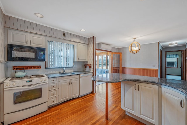 kitchen with wainscoting, light wood-style floors, white appliances, a wall mounted AC, and a sink