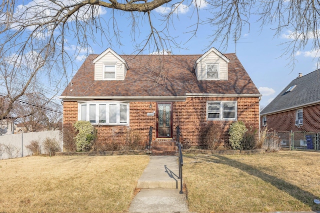 cape cod-style house with brick siding, roof with shingles, a front yard, and fence