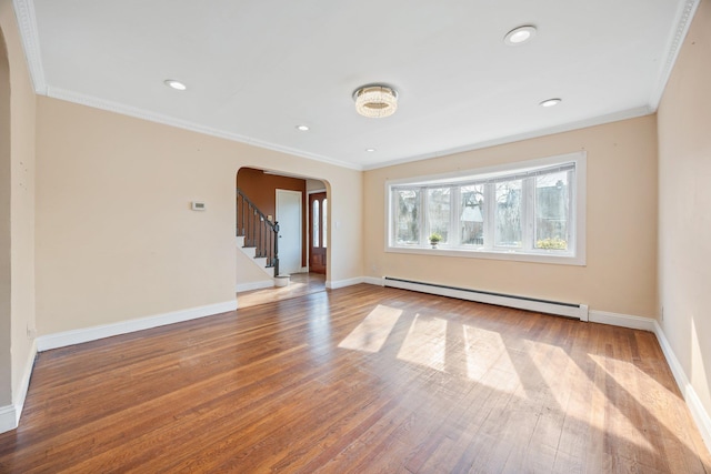 empty room with a baseboard heating unit, arched walkways, ornamental molding, and hardwood / wood-style flooring