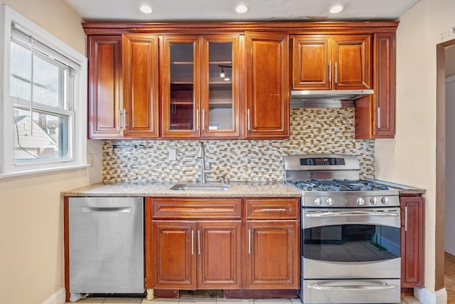 kitchen featuring a sink, stainless steel appliances, glass insert cabinets, under cabinet range hood, and backsplash