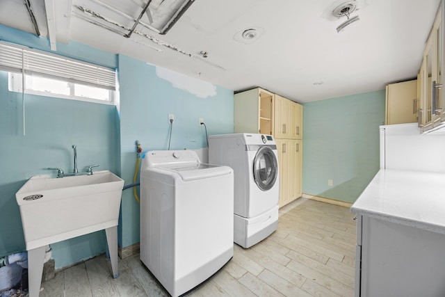 laundry area with cabinet space, light wood-style flooring, and separate washer and dryer