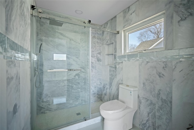 bathroom featuring a marble finish shower, toilet, and tile walls