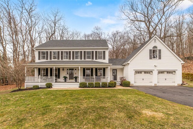 colonial inspired home featuring aphalt driveway, roof with shingles, covered porch, and a front lawn