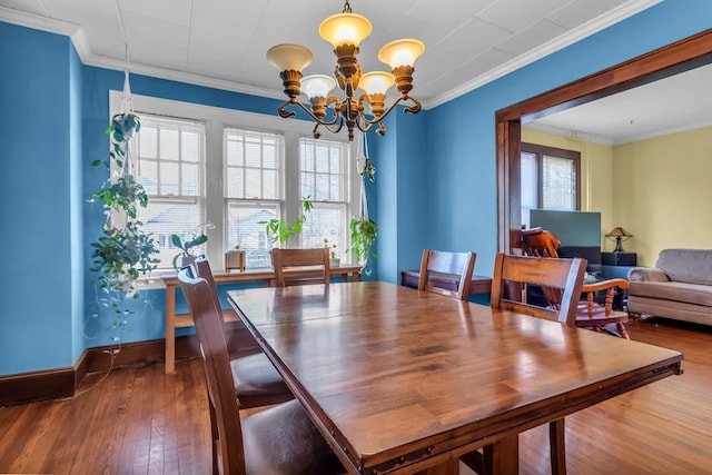 dining space with baseboards, wood-type flooring, a notable chandelier, and crown molding