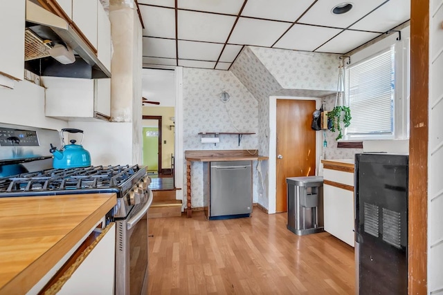 kitchen featuring wallpapered walls, butcher block countertops, stainless steel appliances, under cabinet range hood, and white cabinetry