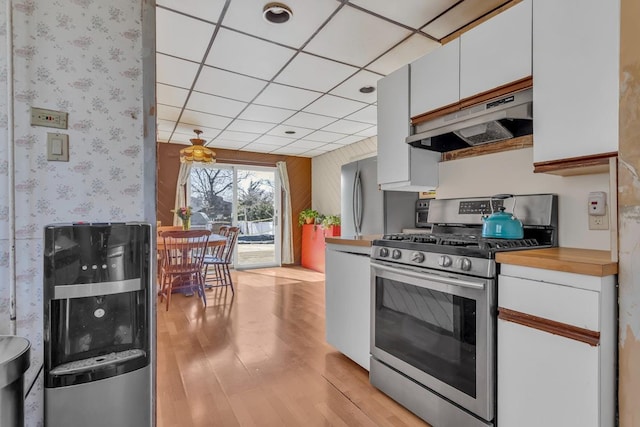 kitchen with gas stove, white cabinets, light wood-style floors, a paneled ceiling, and under cabinet range hood