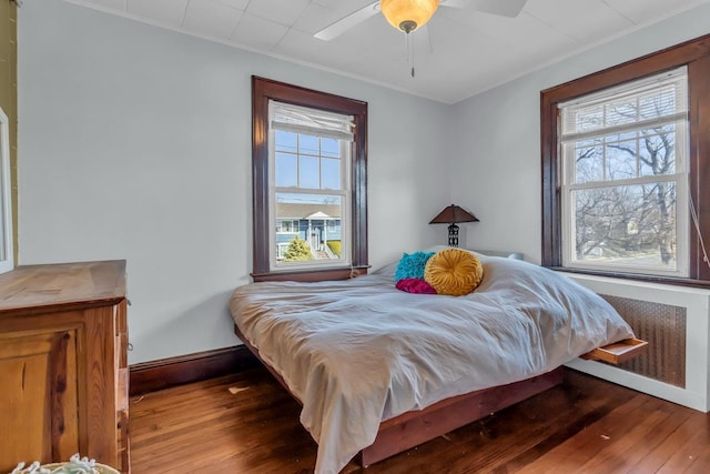 bedroom with baseboards, multiple windows, radiator, and wood-type flooring