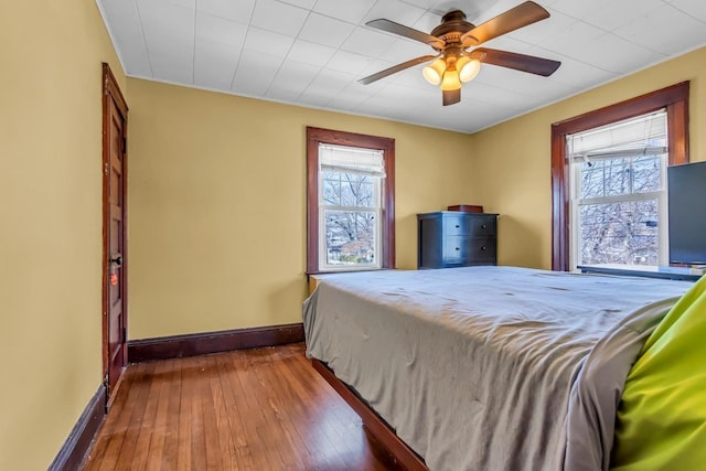 unfurnished bedroom with hardwood / wood-style flooring, multiple windows, baseboards, and ceiling fan