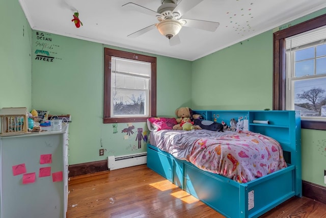 bedroom featuring a ceiling fan, a baseboard heating unit, wood finished floors, crown molding, and baseboards